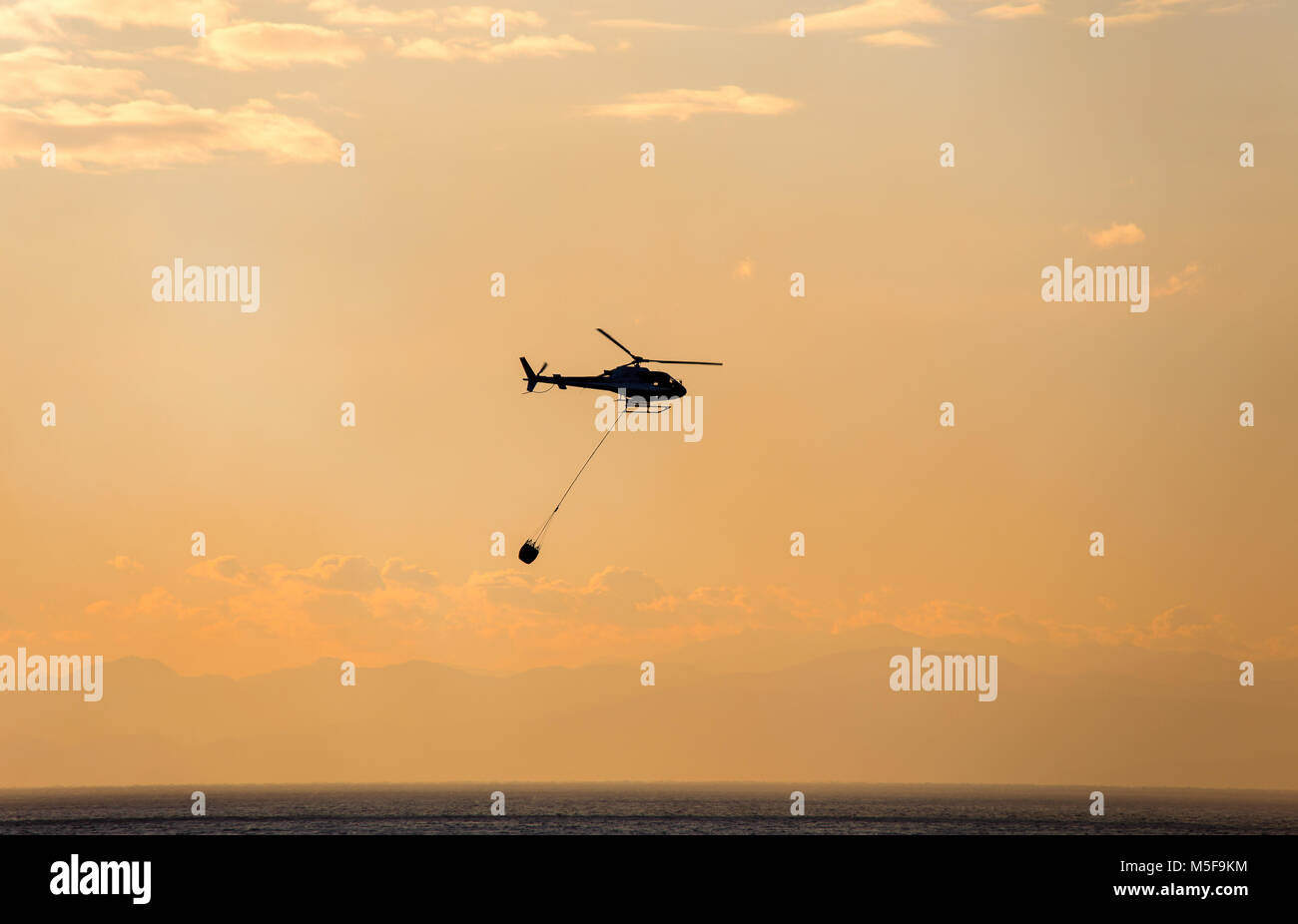 Der Helikopter sammelt das Wasser aus dem Meer, um einen Brand zu löschen Stockfoto