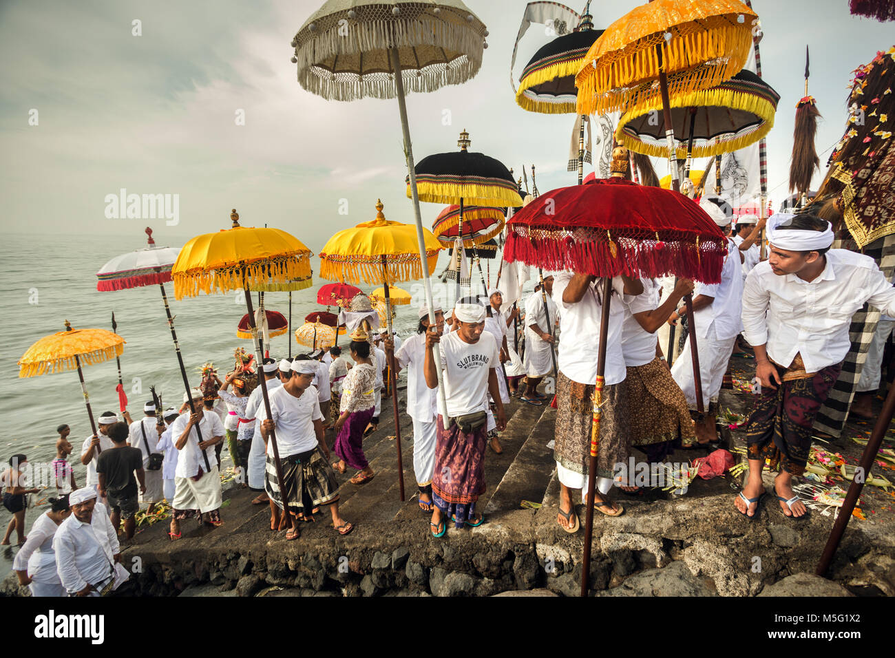 Religiöse Versammlung und religiösen Masse der balinesischen Hindu's mit bunten Religiösen sonnenschirme Melasti Zeremonie auf einer Bali Beach. Traditionelle Rituale Stockfoto
