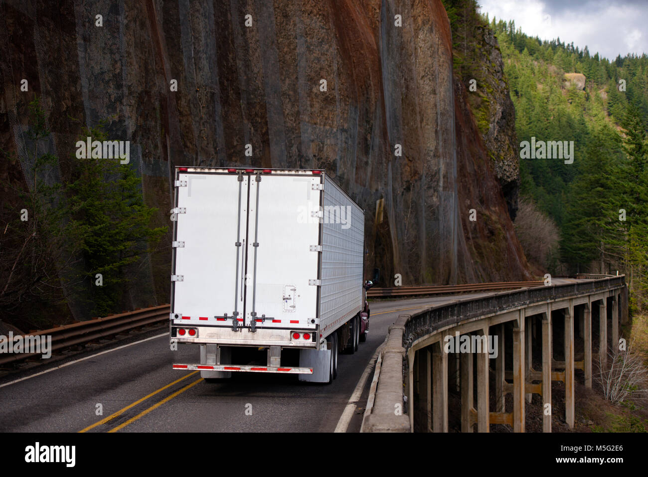 Big Rig Semi Truck mit langen Kühlschrank Auflieger tragen der kommerziellen Ladung und Bewegen auf Brücke mit Hilfs Stangen an der Seite der große Wand in Colu Stockfoto
