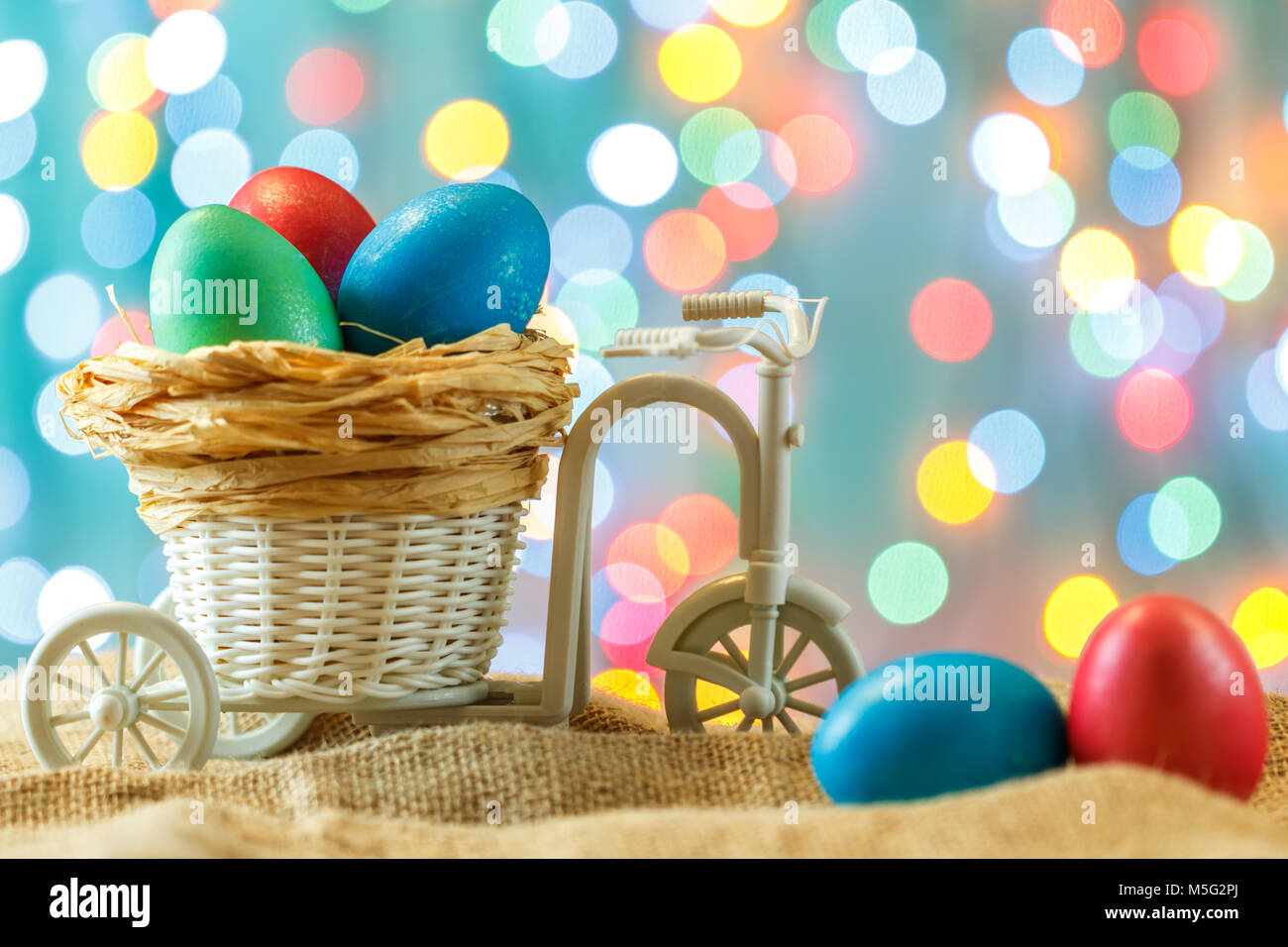 Ostern Karte, farbige Eier im Nest. Spielzeug Fahrrad mit einer Karre. Frohe Ostern. Zarte blau Hintergrund. Für Text platzieren. Stockfoto