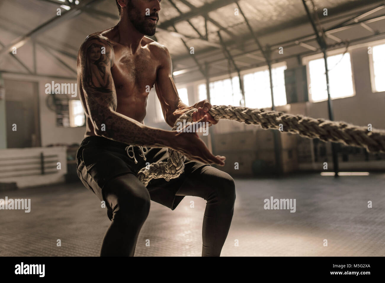 Athletischer Mann mit großen Körperbau Seil ziehen. Starke mann Ziehen von schweren Seil Cross Training Gym. Stockfoto