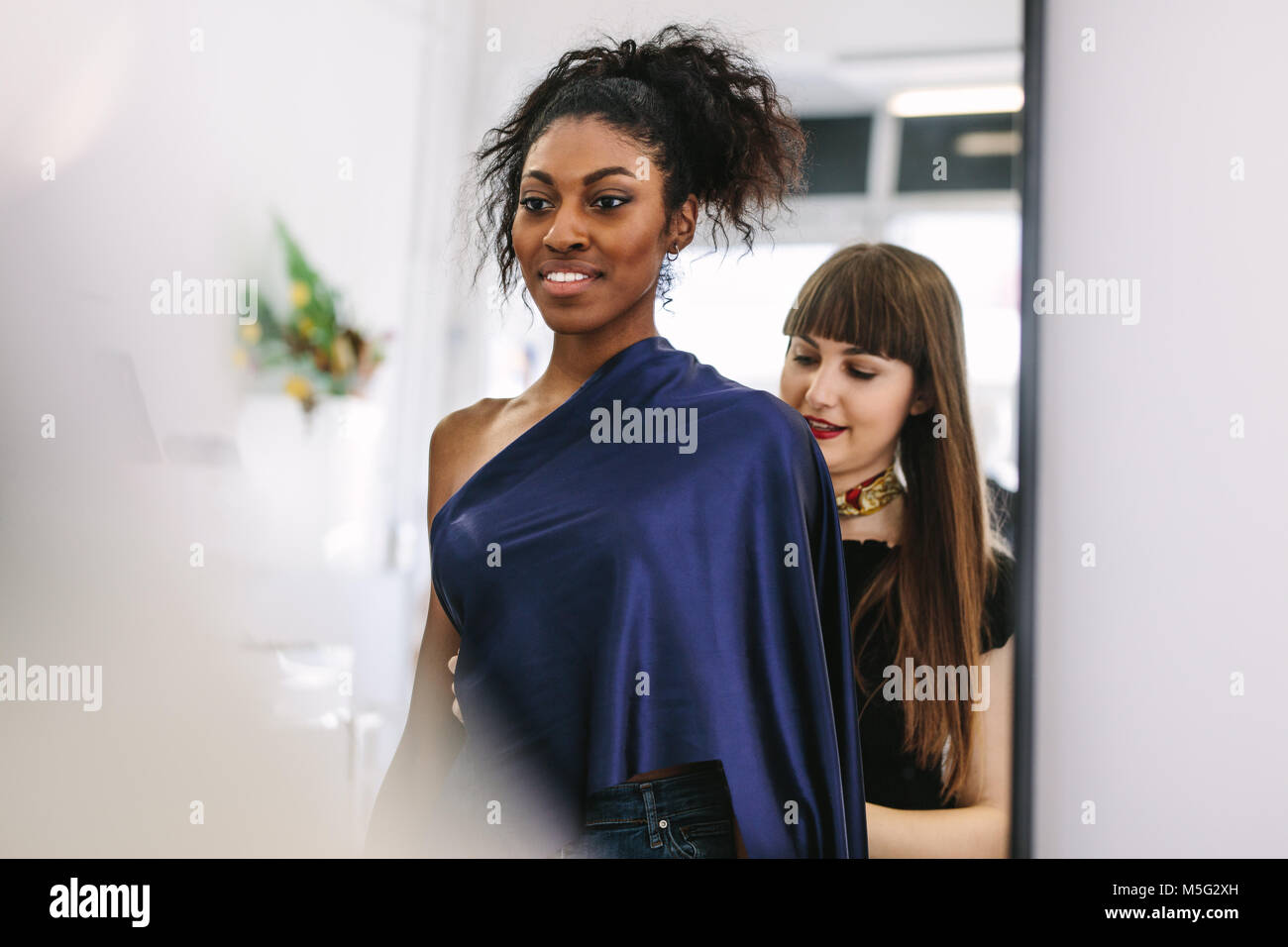 Young Fashion Designer arbeiten an ihren Entwürfen mit einem Modell. Frau Unternehmer in ihr Tuch Shop Design neuer Kleidung. Stockfoto