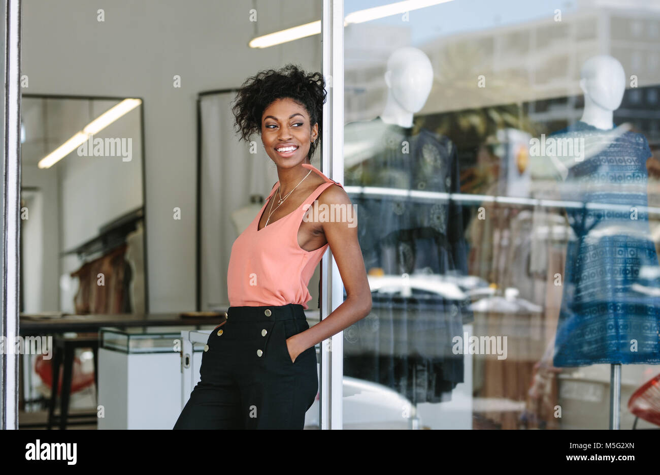 Lächelnd kleid designer in ihr Tuch Shop mit Designer Kleidung auf dem Display. Frau Unternehmer am Eingang ihre Mode Studio. Stockfoto