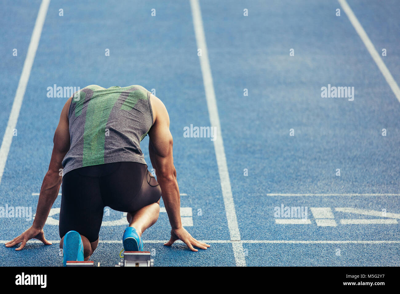 Rückansicht eines Athleten bereit auf einem All-Wetter Laufstrecke zu sprinten. Läufer mit einem startblock seinen Lauf auf der Rennstrecke zu starten. Stockfoto