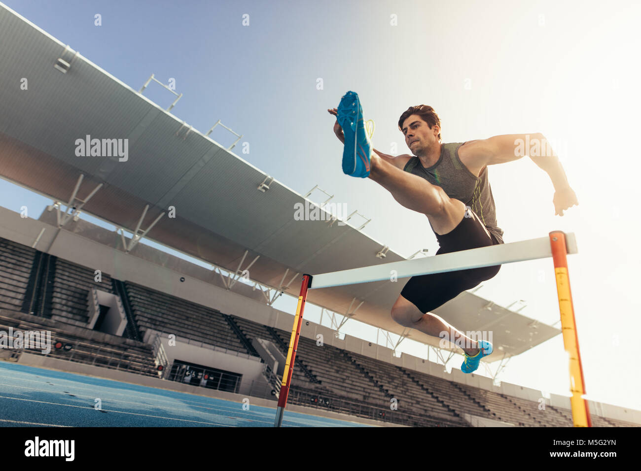 Nahaufnahme von einem Läufer einen Sprung über eine Hürde bei der Schiene und im Feld Ereignis. Athleten, die eine Hürde Rennen in einem Stadion. Stockfoto