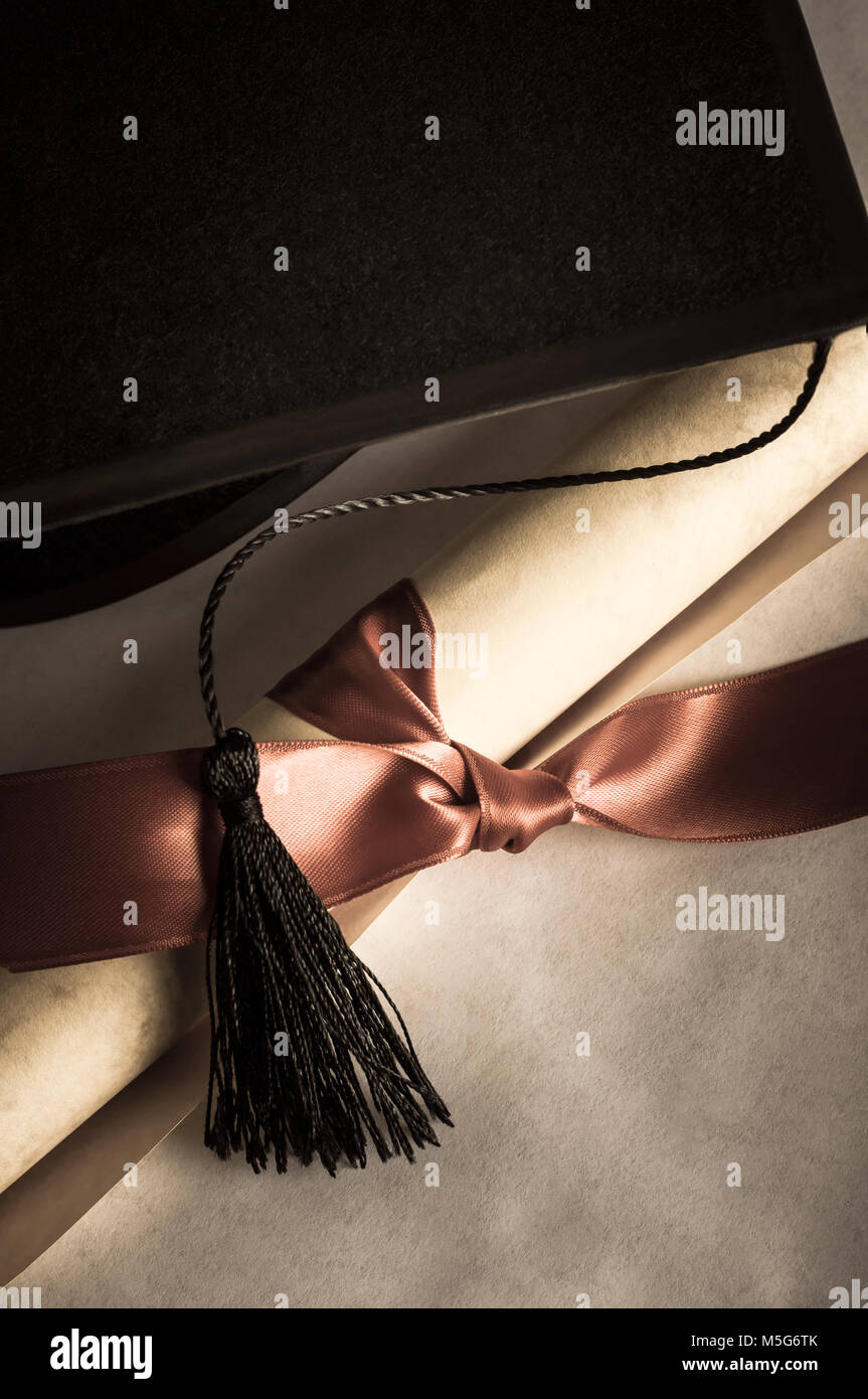 Nahaufnahme von einem schwarzen mortarboard mit Quaste hing über aufgerollte Pergament blättern, mit roter Schleife gebunden. Für vintage Aussehen Undersaturated. Stockfoto