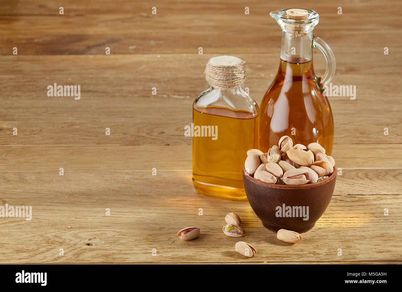 Zusammensetzung der aromatischen Öl in einem Glas und Flasche mit ungeschälte Pistazien in der Schale auf Holztisch, close-up. Nahrhafte therapeutische Nahrung für Heilen Stockfoto