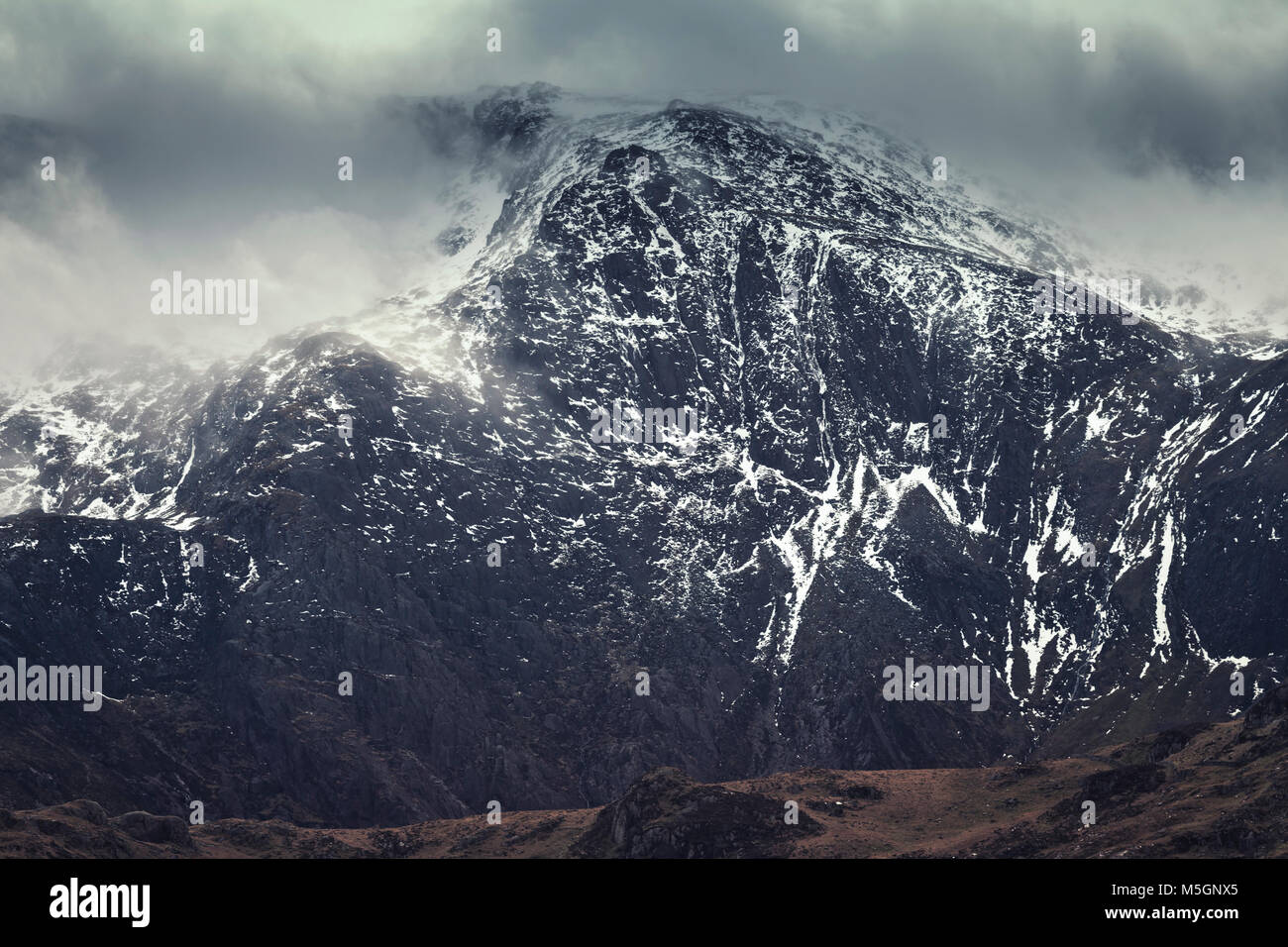 Malerische Berg in dramatische Wolken im Winter schneebedeckten Gipfel. Snowdonia National Park in Nord Wales, Großbritannien Stockfoto
