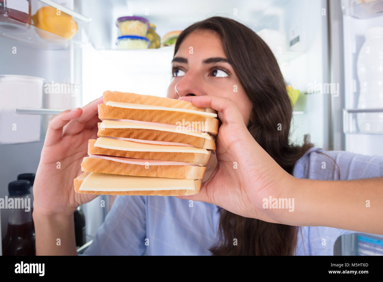 Nahaufnahme einer jungen Frau Essen Sandwich Vor Kühlschrank Stockfoto