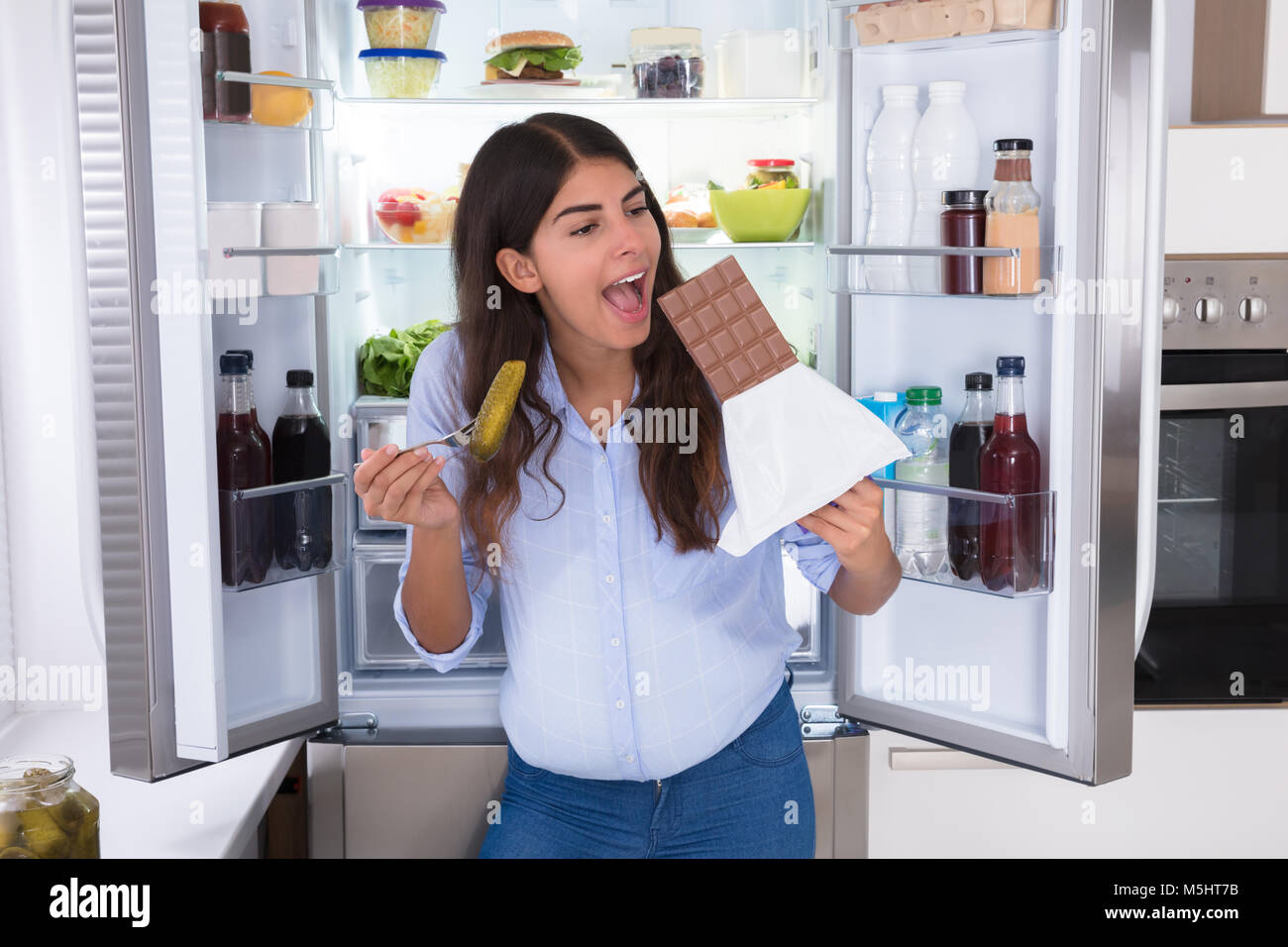 Junge Frau Schokolade essen in der Nähe von offenen Kühlschrank Stockfoto