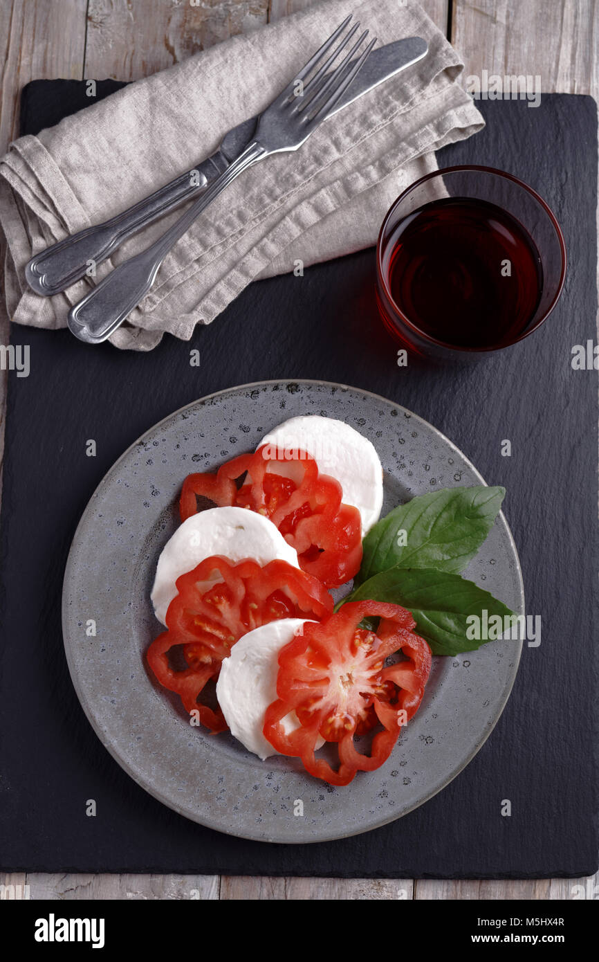 Caprese Salat mit Mozzarella, Tomaten und Basilikum und einem Glas Rotwein auf einem rustikalen Tisch Stockfoto