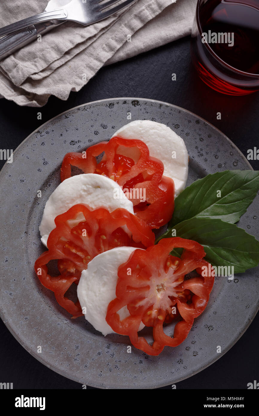 Caprese Salat mit Mozzarella, Tomaten und Basilikum und einem Glas Rotwein auf einem rustikalen Tisch Stockfoto