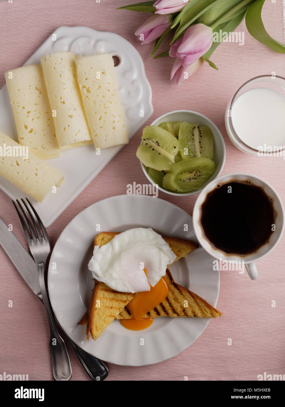 Muttertag Frühstück mit pochiertem Ei, Toast, Käse, Milch, Kaffee, geschnittene Kiwis und ein Bündel von Tulpen Stockfoto