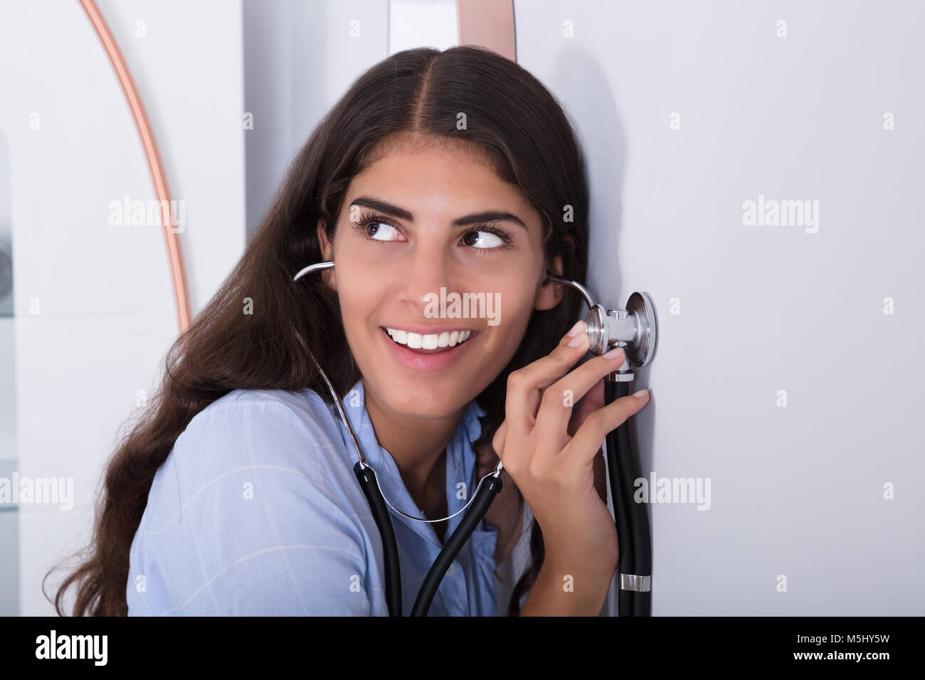 Junge neugierige Frauen hören durch Wand mit Stethoskop Stockfoto