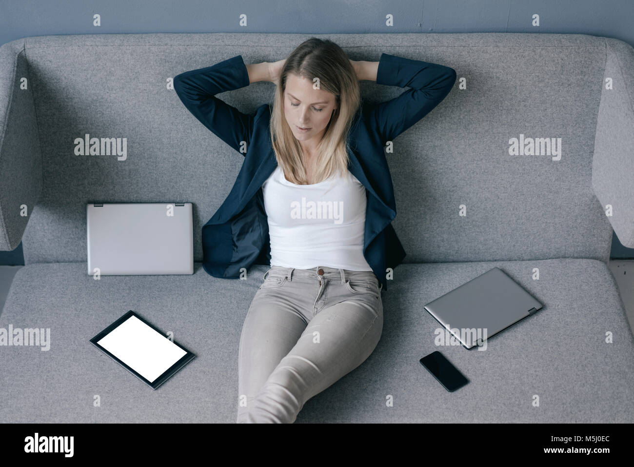Geschäftsfrau, sitzen auf der Couch mit mehreren elektronischen Geräten entspannend Stockfoto