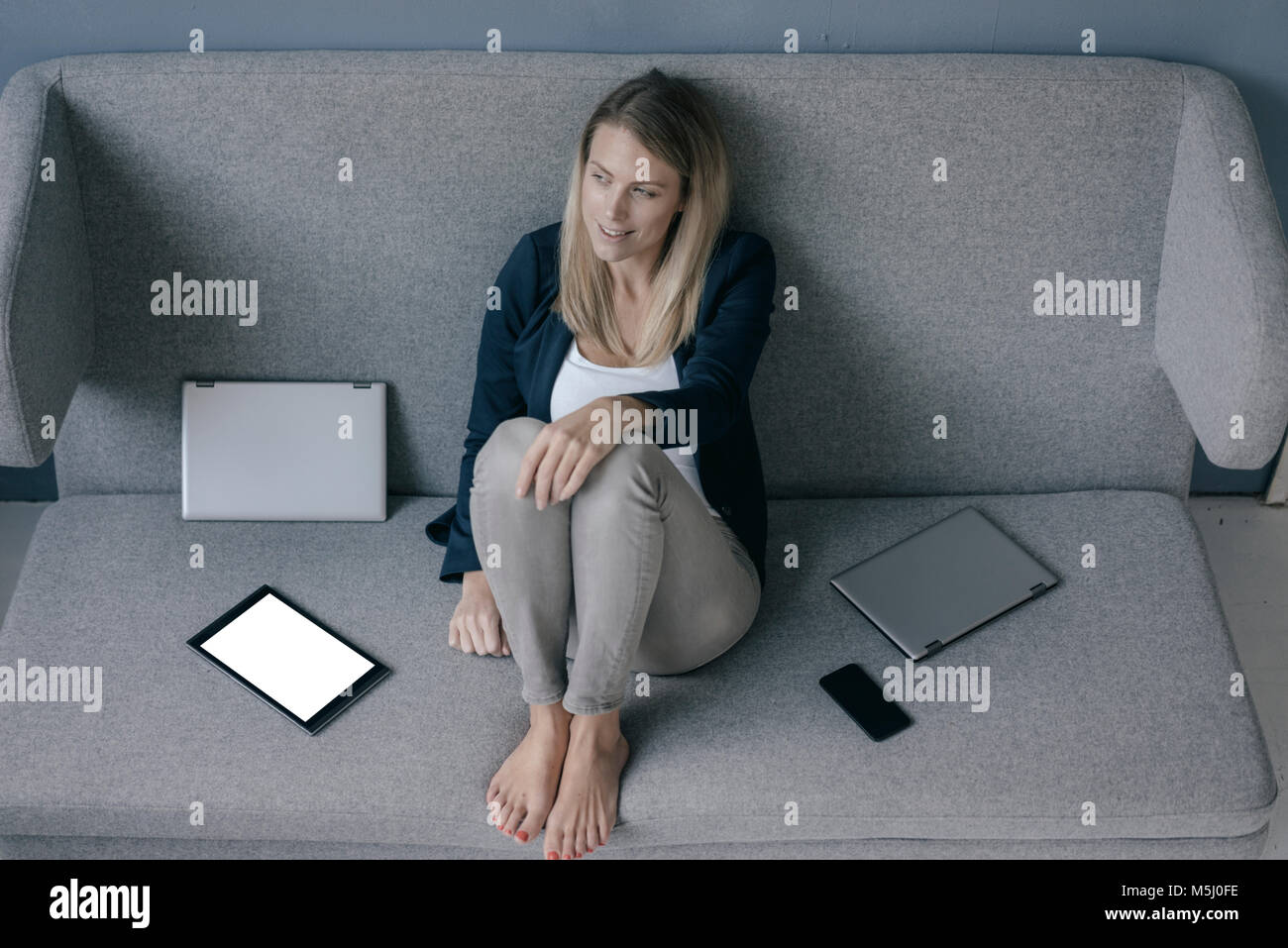Lächeln, Geschäftsfrau, sitzen auf der Couch mit mehreren elektronischen Geräten entspannend Stockfoto