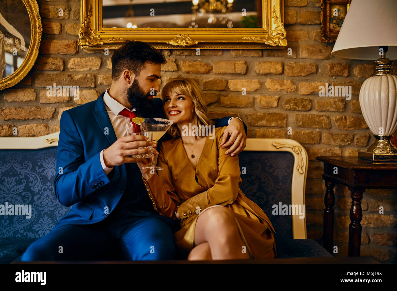 Happy Elegant Paar mit Getränken sitzen auf der Couch umarmt Stockfoto