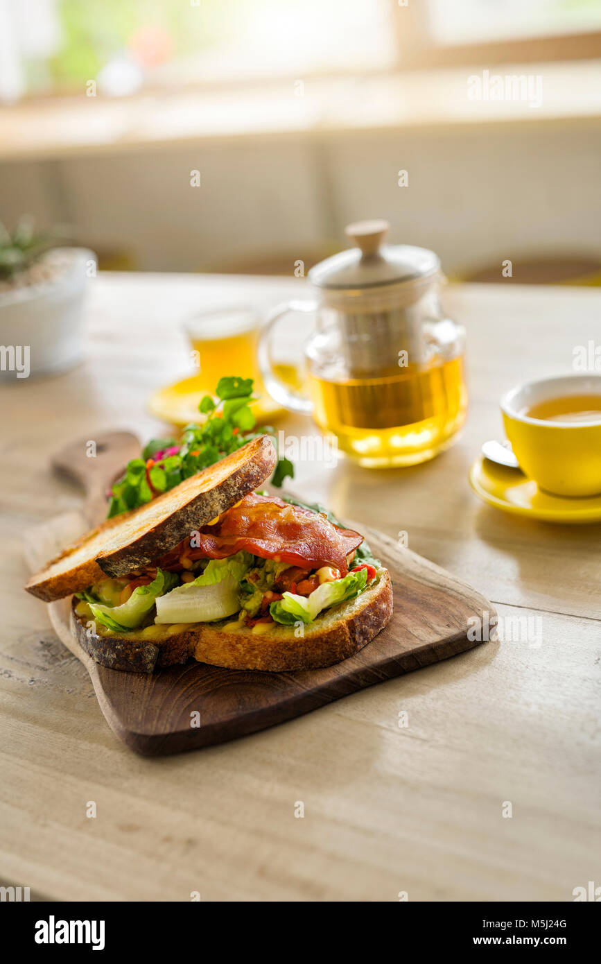 Knuspriges Brot mit grünem Salat und Schinken auf Holzplatte und grüner Tee im Cafe Stockfoto