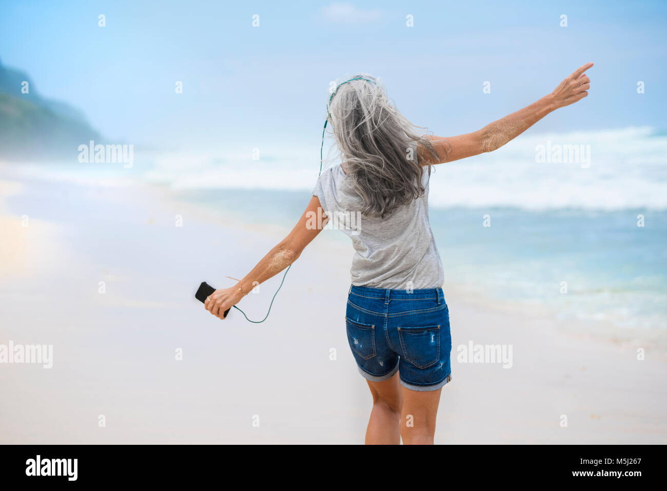 Ältere Frau mit Kopfhörer tanzen am Strand Stockfoto