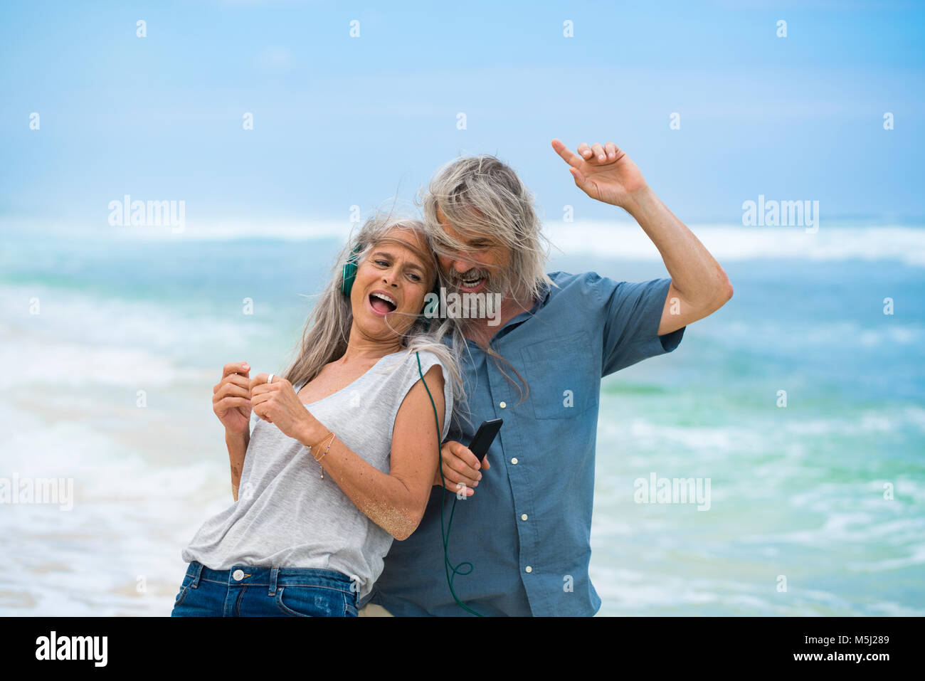 Schönes älteres Ehepaar mit Kopfhörer tanzen am Strand Stockfoto
