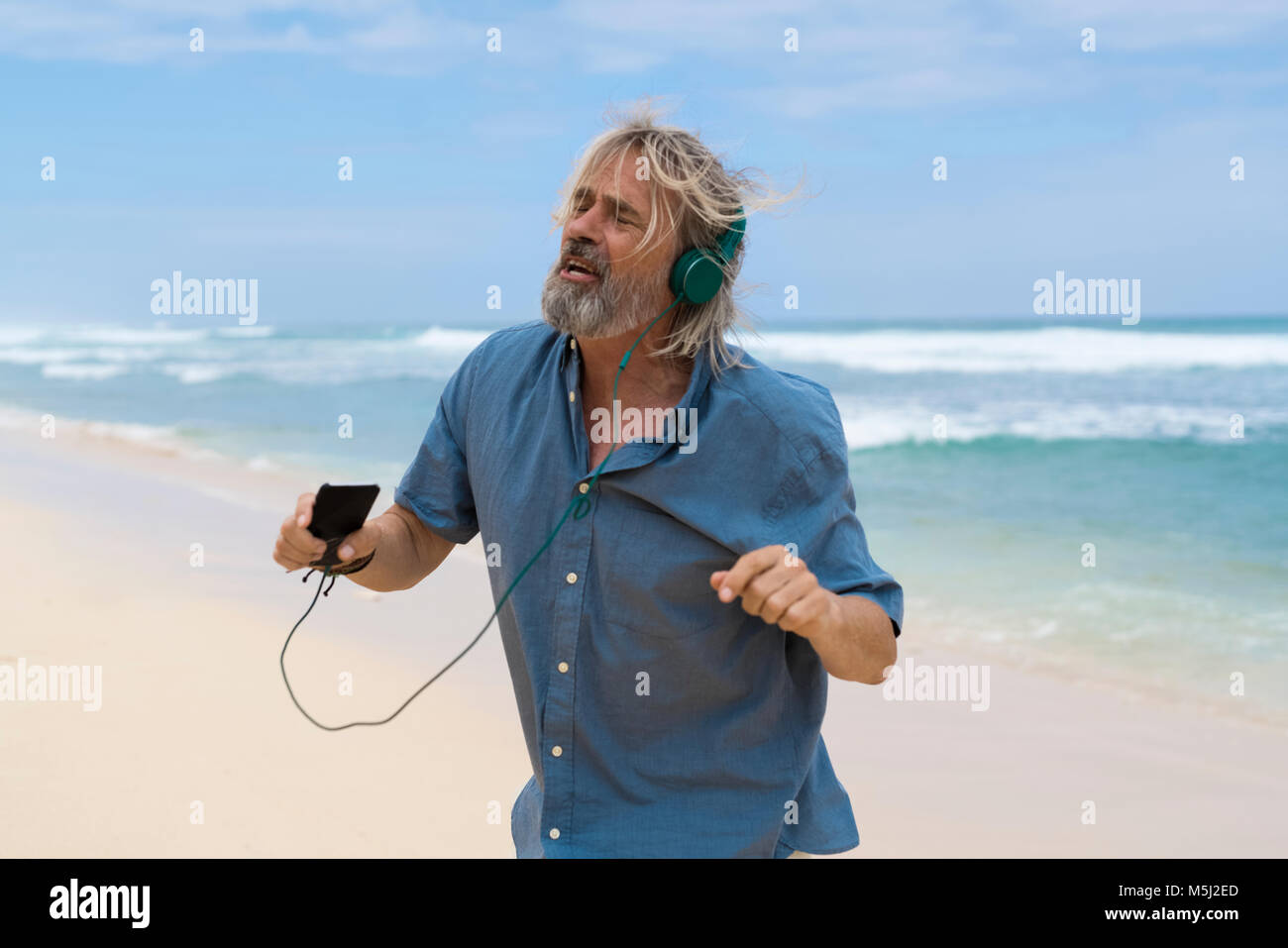 Gut aussehender älterer Mann mit Kopfhörer tanzen am Strand Stockfoto