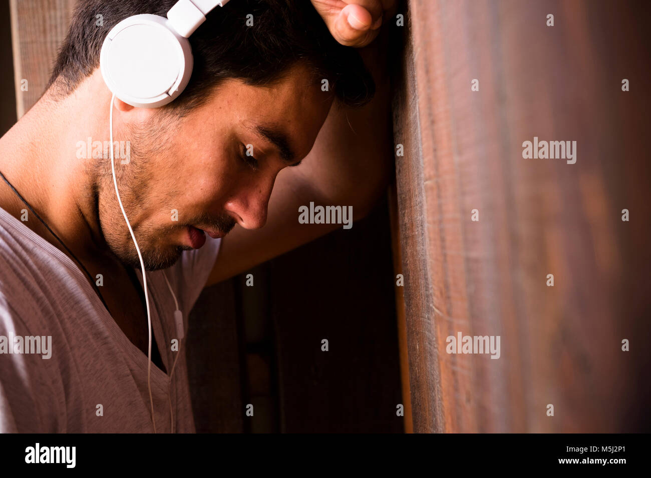 Ernsthaften jungen Mann mit Kopfhörern gegen Holz Wand lehnt Stockfoto