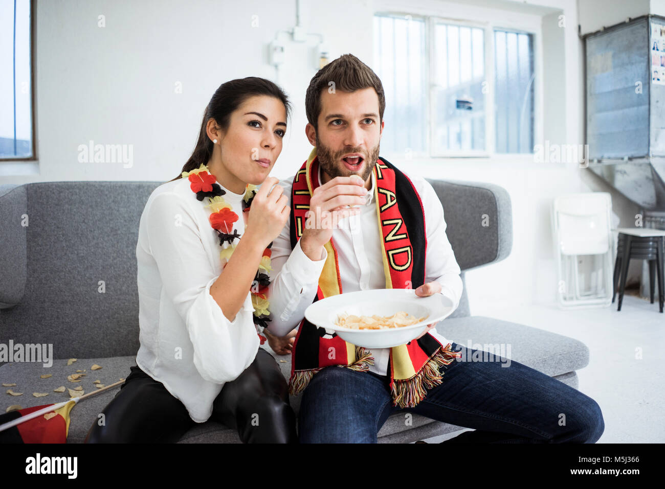 Deutscher Fußball-Fan Paar sitzt auf der Couch Chips essen und Fernsehen Stockfoto