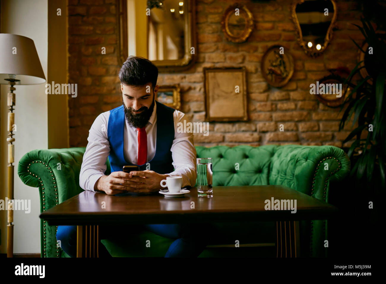 Modische junge Mann sitzt am Tisch in einem Cafe mit Handy Stockfoto