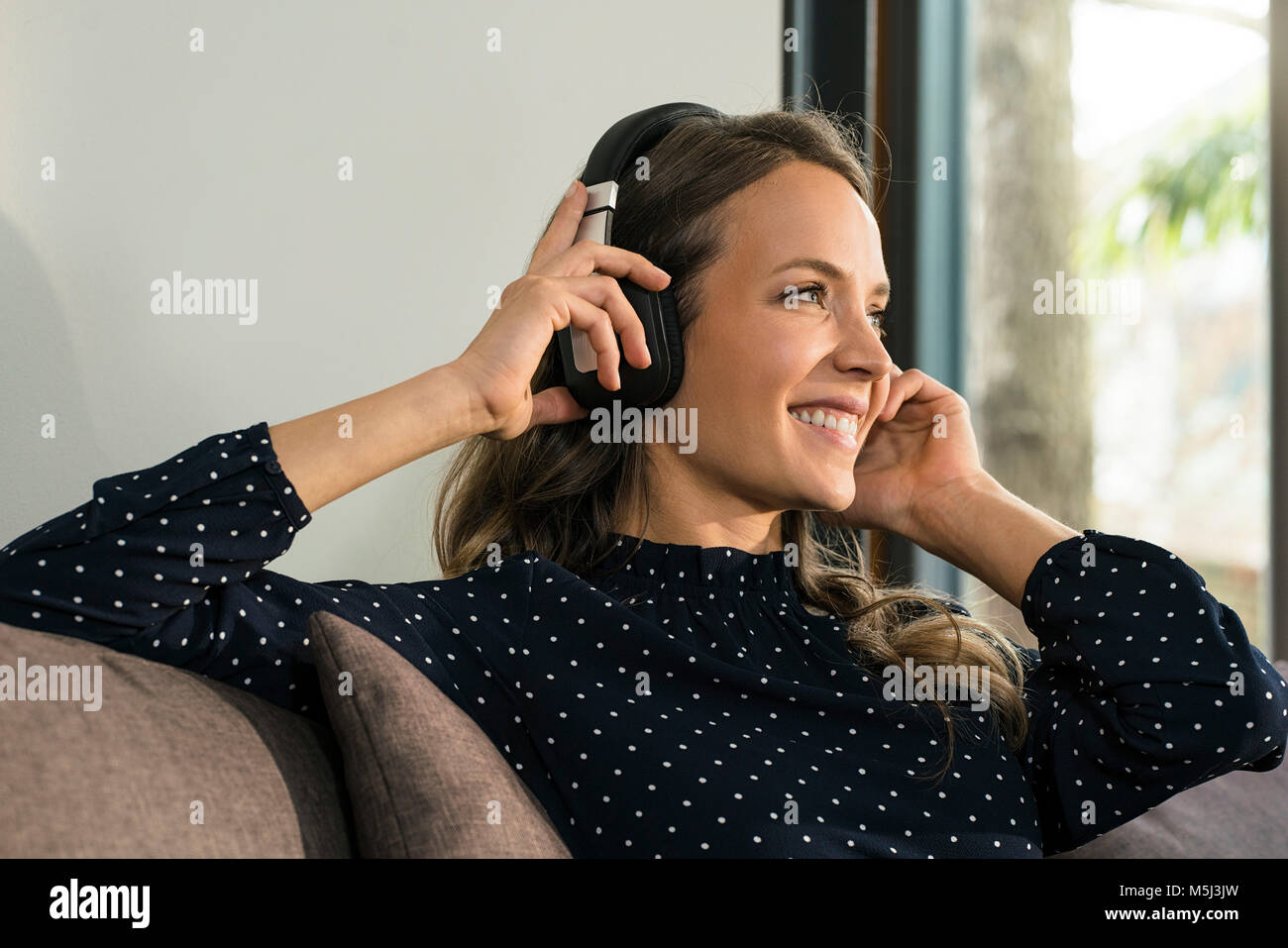 Lächelnde Frau mit Kopfhörern entspannt auf der Couch zu Hause Stockfoto