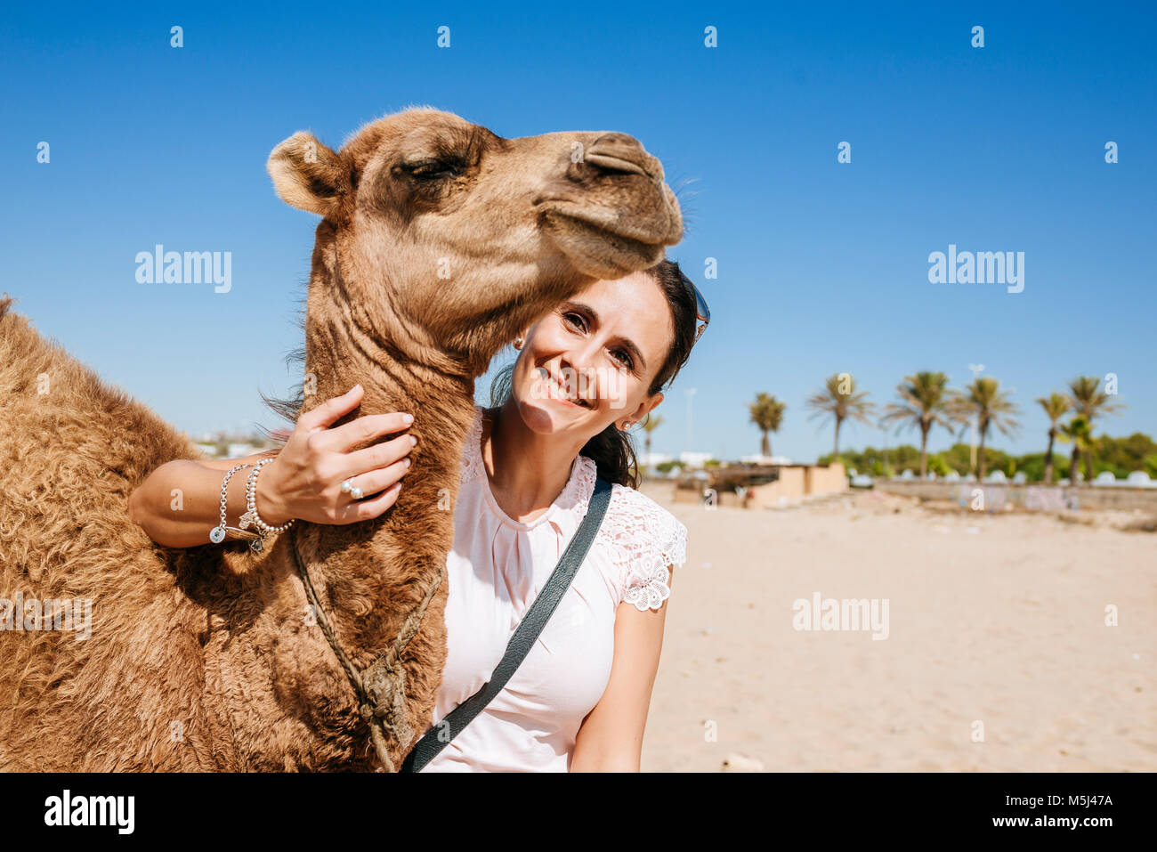 Marokko, Tanger, Porträt der lächelnde Frau mit Baby Kamel am Strand Stockfoto