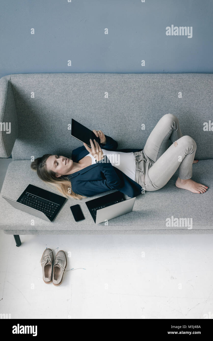 Geschäftsfrau auf der Couch liegen mit mehreren elektronischen Geräten über Tablet Stockfoto