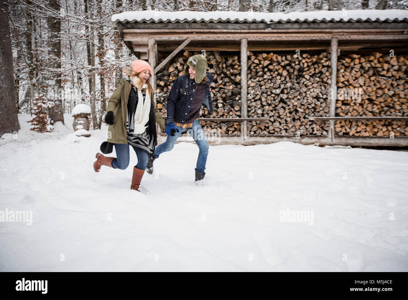 Glückliches Paar läuft vor der Holzstapel im Winter Stockfoto