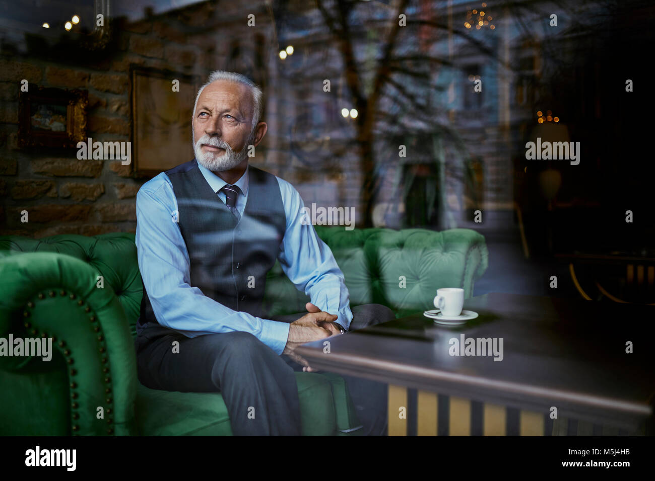 Elegante älterer Mann sitzt am Tisch in einem Cafe Blick aus Fenster Stockfoto