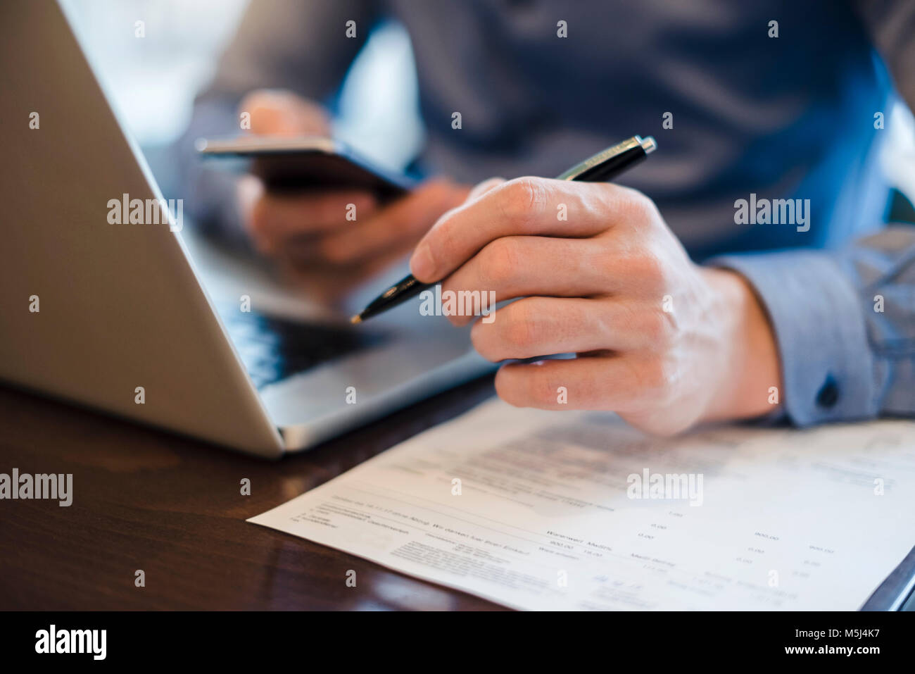 Mann an Schreibtisch mit Handy und Kugelschreiber in der Hand, Nahaufnahme Stockfoto