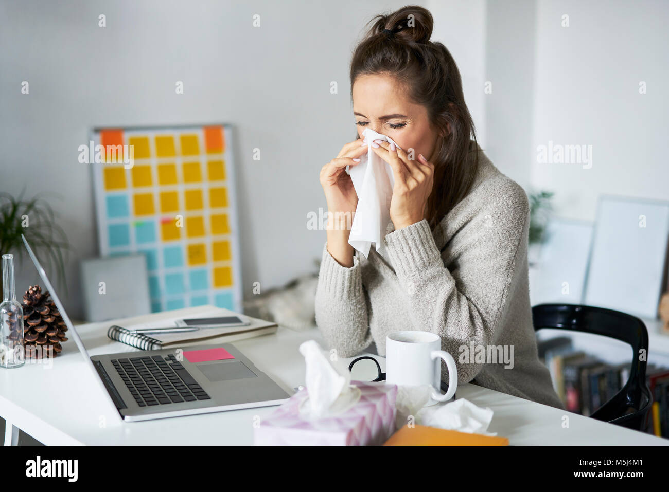 Kranke Frau zu Hause am Schreibtisch ihre Nase weht Stockfoto