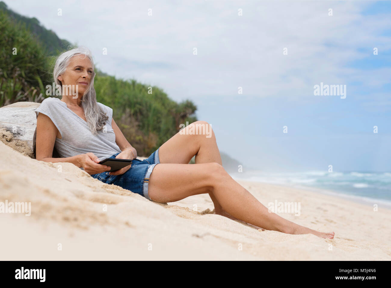 Schönen Lächeln ältere Frau am Strand liegend, Holding e-book Stockfoto