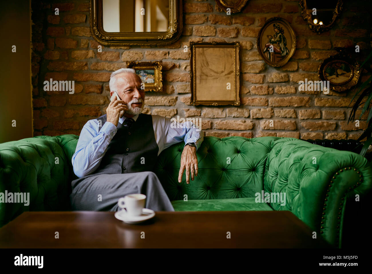 Elegante älterer Mann sitzt am Tisch in einem Cafe mit Handy Stockfoto