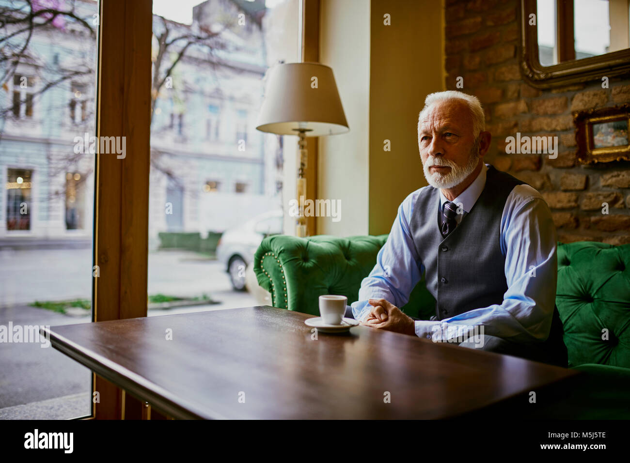 Elegante älterer Mann sitzt am Tisch in einem Cafe Stockfoto