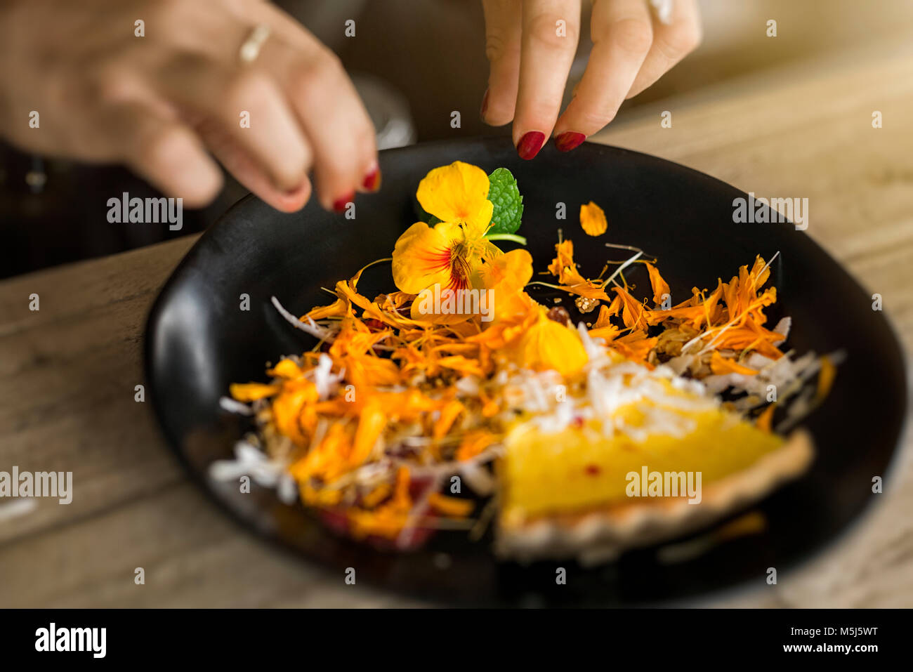 Weibliche Hände mit rotem Nagellack Kuchen dekorieren mit Blumen Stockfoto