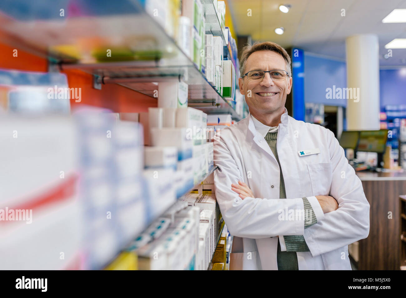 Portrait von lächelnden Apotheker lehnen gegen Regal mit Medikament in der Apotheke Stockfoto