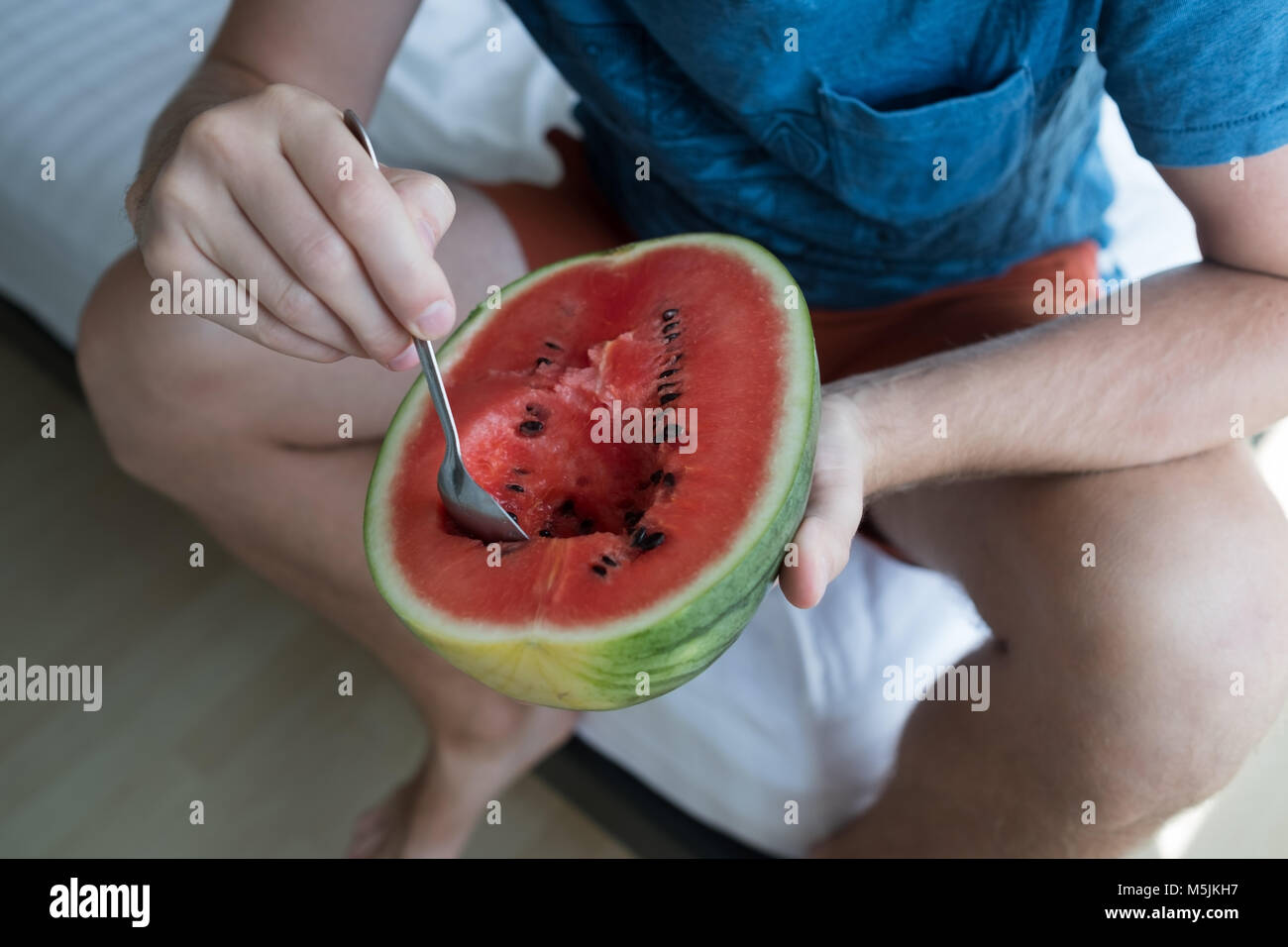 Junger Mann essen eine Wassermelone zu Hause mit Löffel Stockfoto