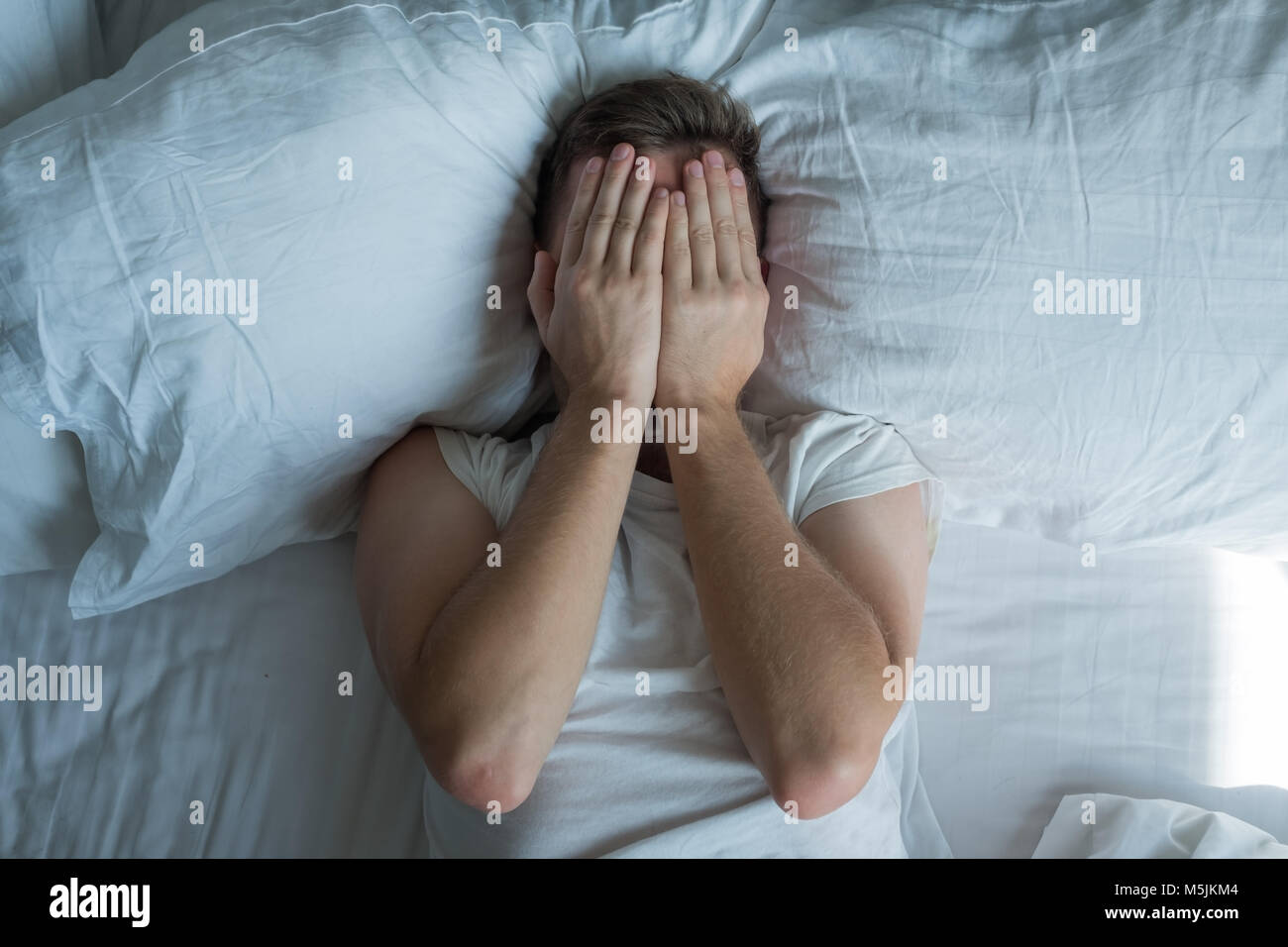 Kaukasischen jungen Mann geschlossenen Augen mit den Händen im Bett Stockfoto