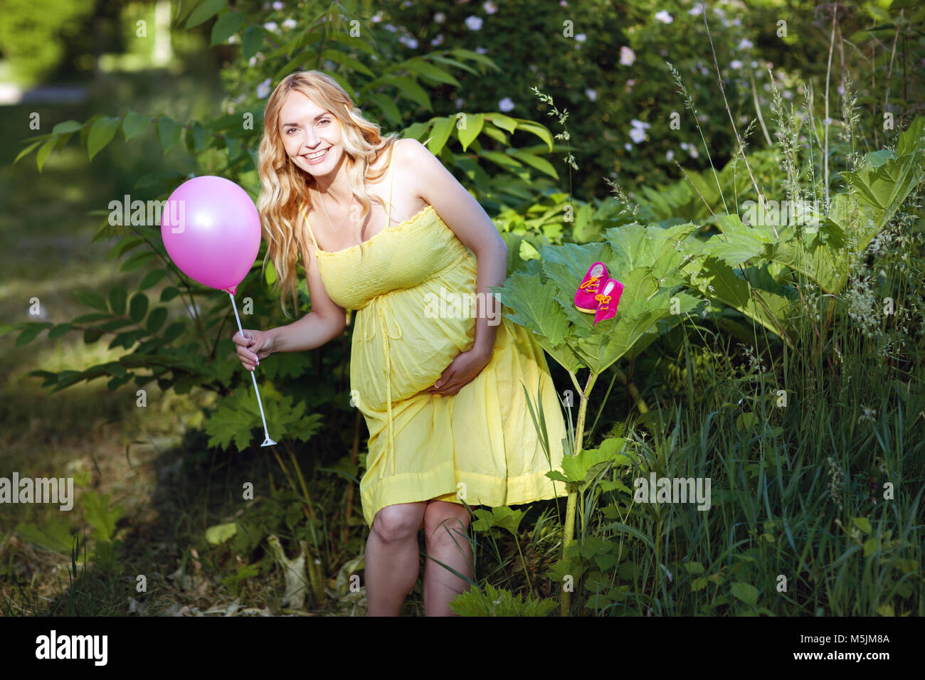 Schöne schwangere Frau steht in den Park. Sie hält einen Ball in der Hand und lacht Stockfoto