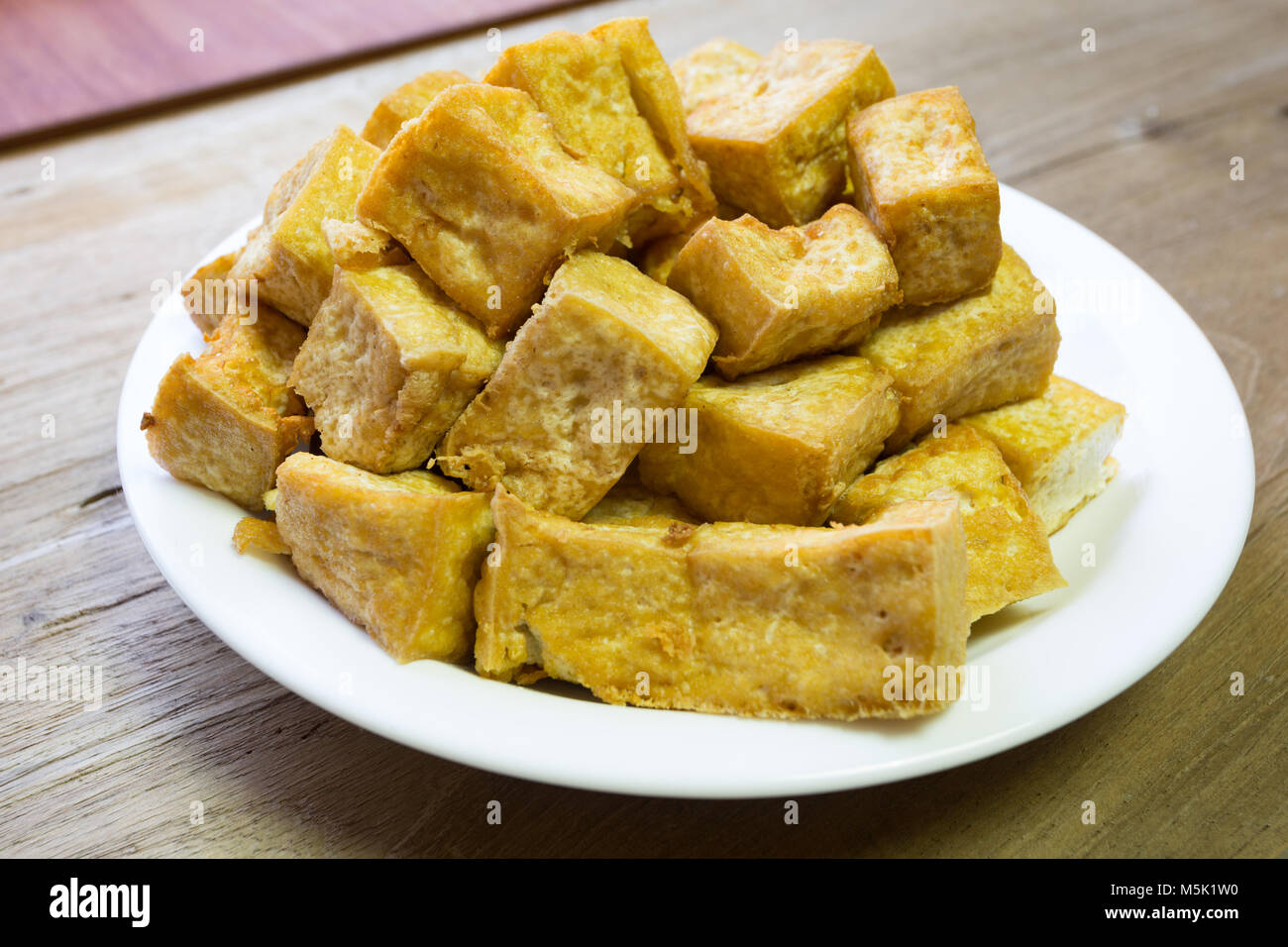 Gebratene weiche Tofu würfeln in weiße Platte auf hölzernen Hintergrund Stockfoto