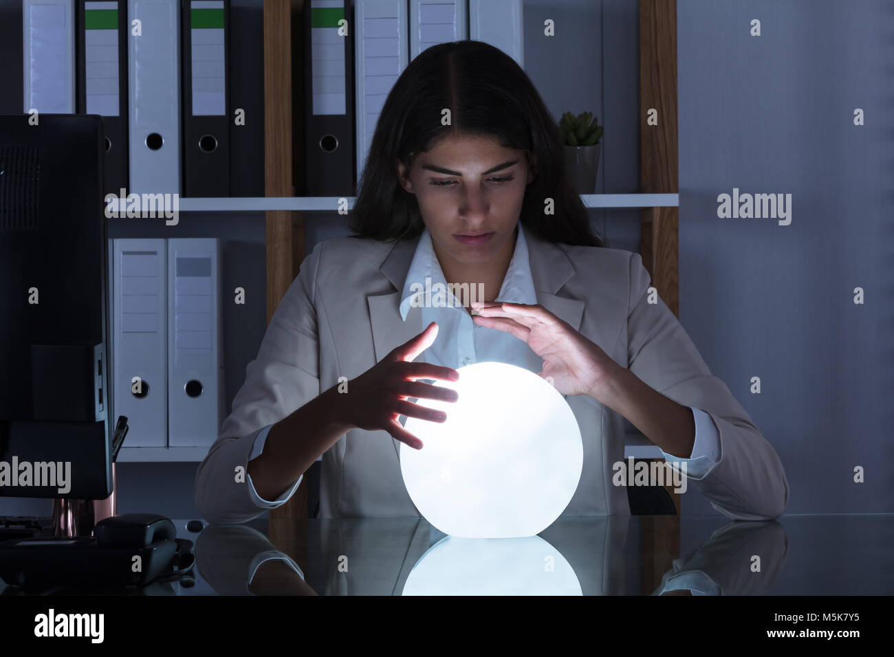 Überarbeitete junge geschäftsfrau Blick in die Zukunft In einer Kristallkugel im Büro Stockfoto