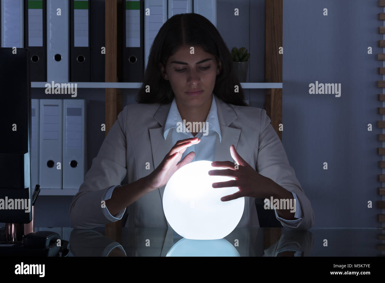 Überarbeitete junge geschäftsfrau Blick in die Zukunft In einer Kristallkugel im Büro Stockfoto