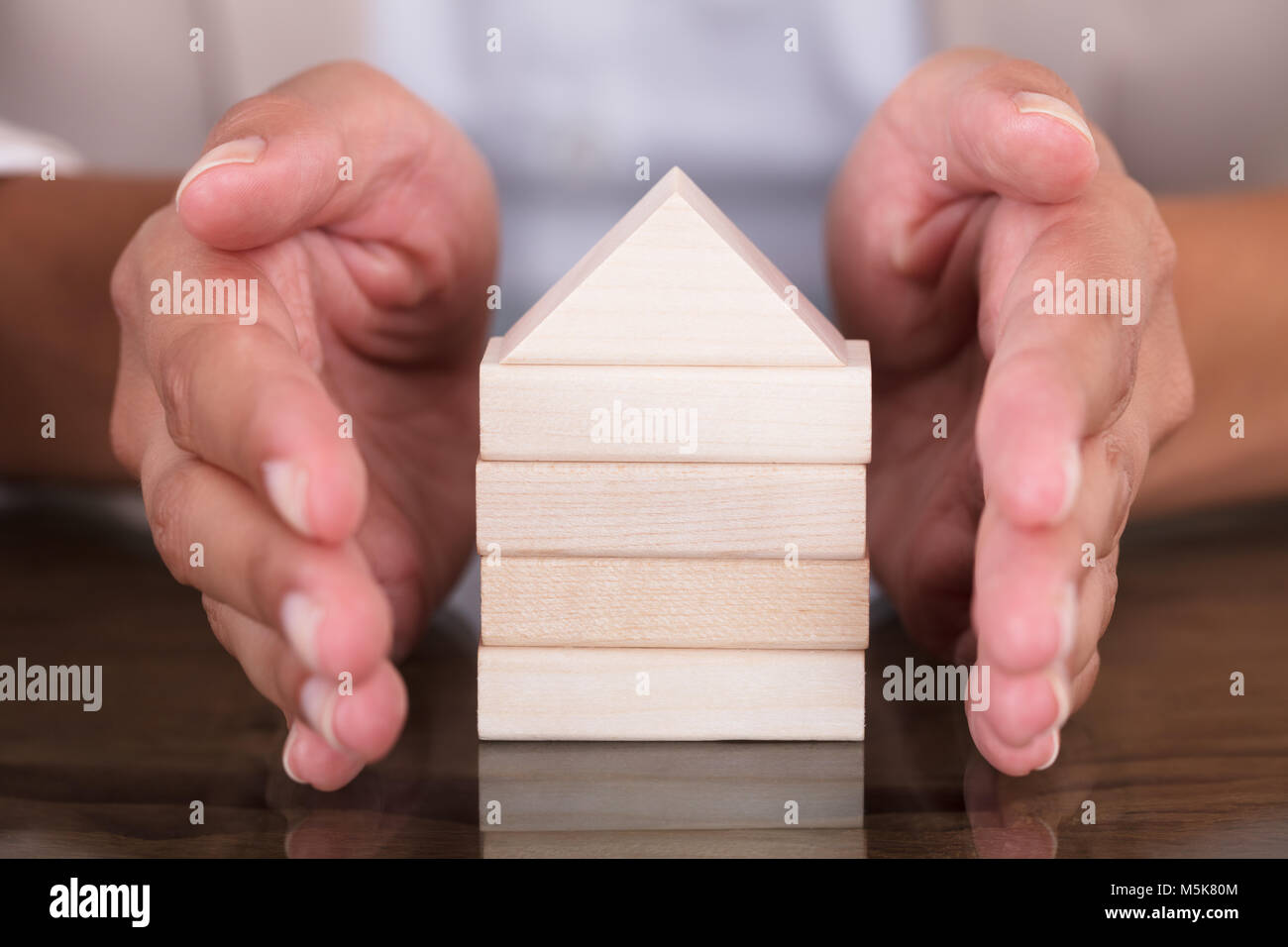 Nahaufnahme der Geschäftsfrau Hand, Modell Home aus Holzklötzen auf Tisch im Büro Stockfoto