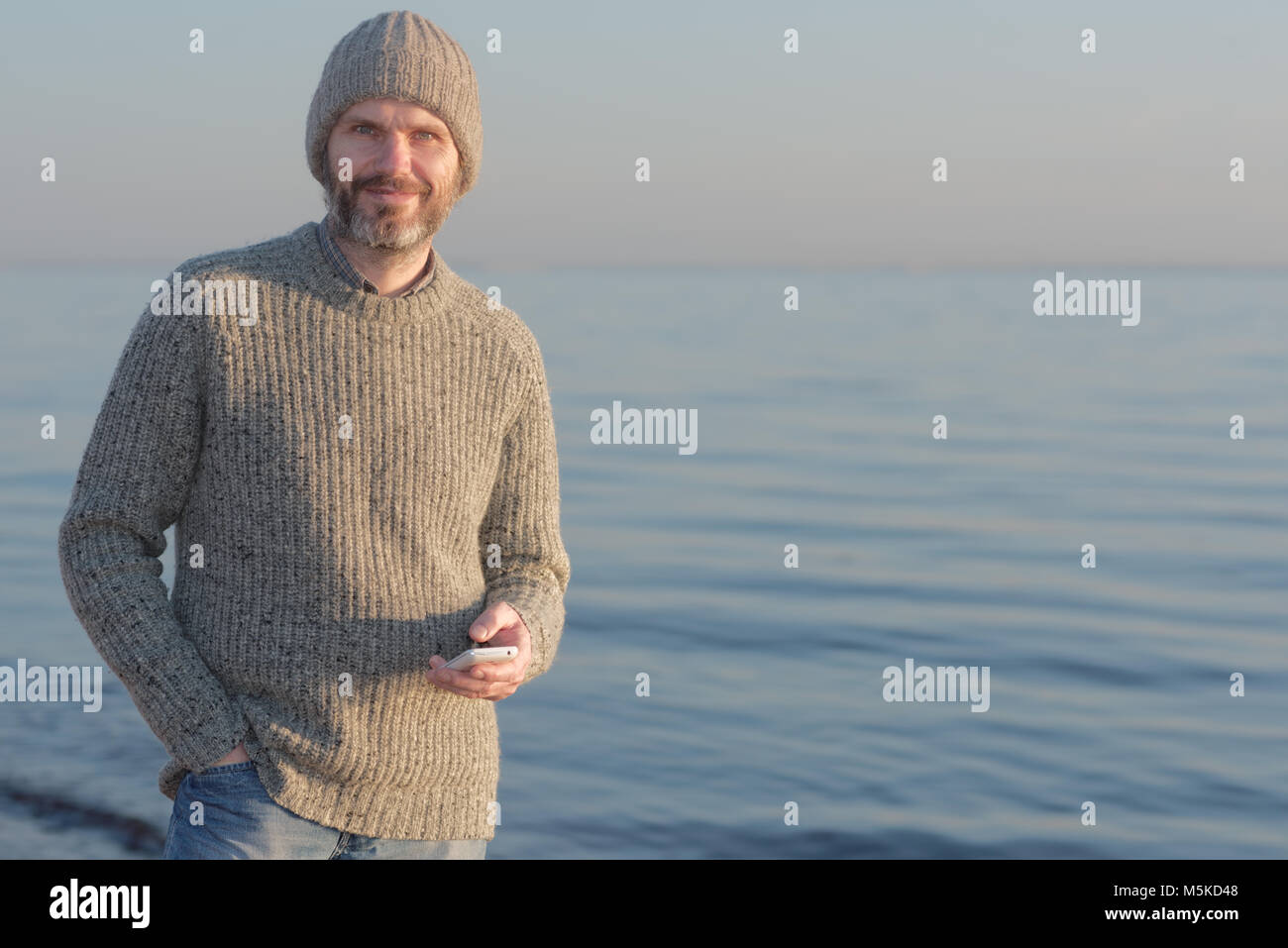 Reifer Mann mit Smartphone gegen ein Meer Stockfoto