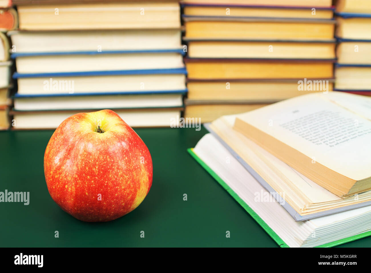 Roter Apfel auf dem grünen Tisch und öffnete Bücher vor dem Hintergrund Stapel Bücher Stockfoto