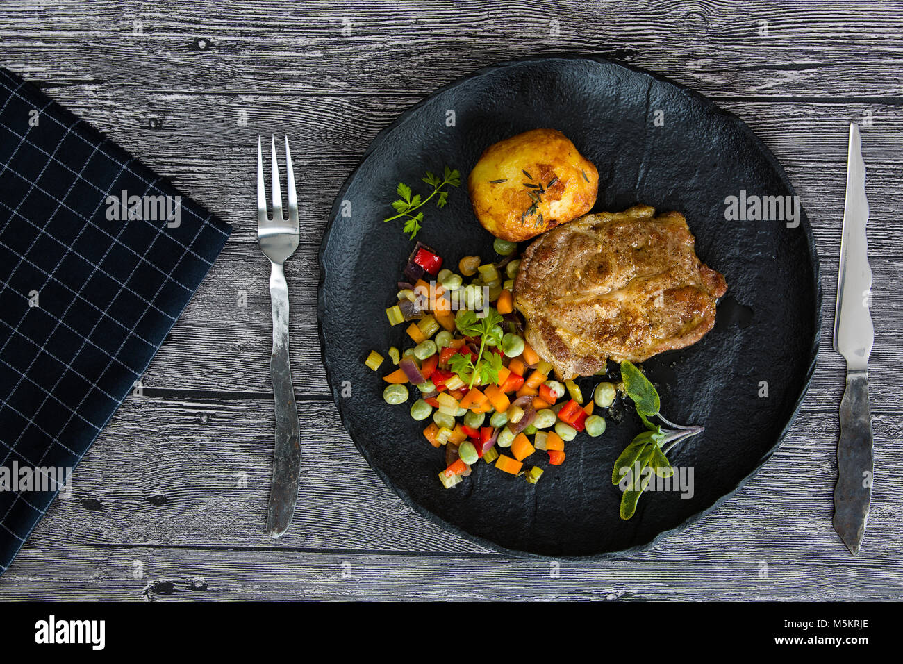 Schweinefleisch vom Grill mit gebratenem Gemüse und gebackene Kartoffel auf einer schwarzen Platte Stockfoto